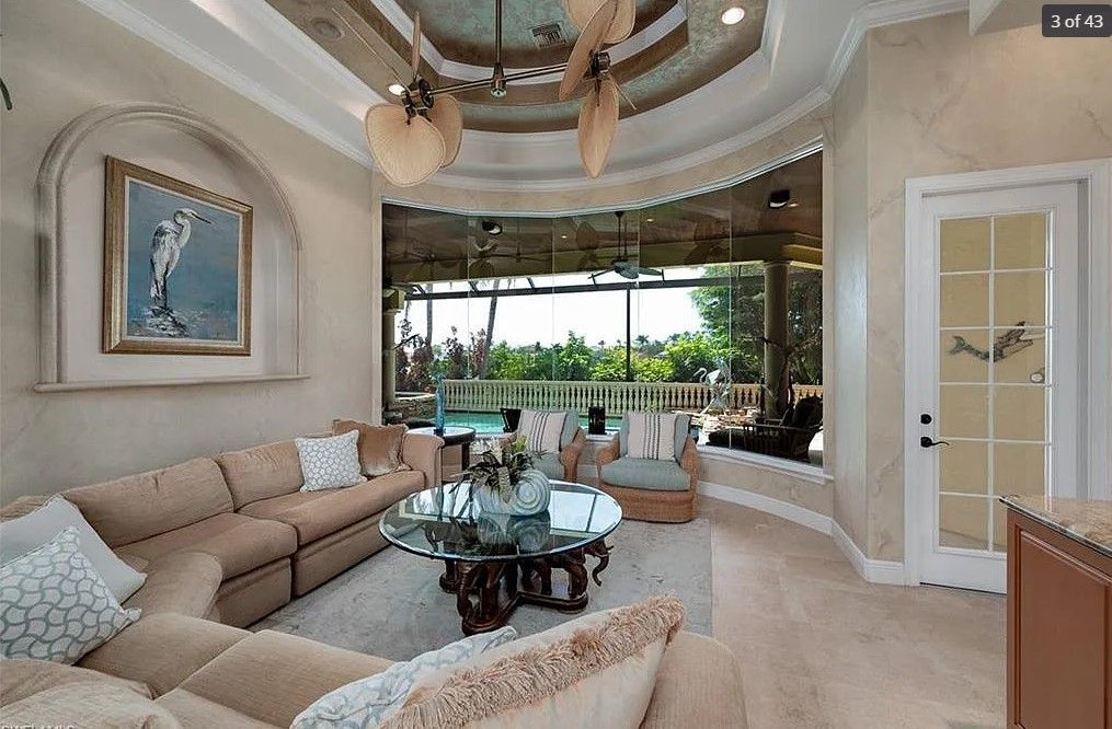 Living room with curved wall, sofa, and glass table overlooking a pool.