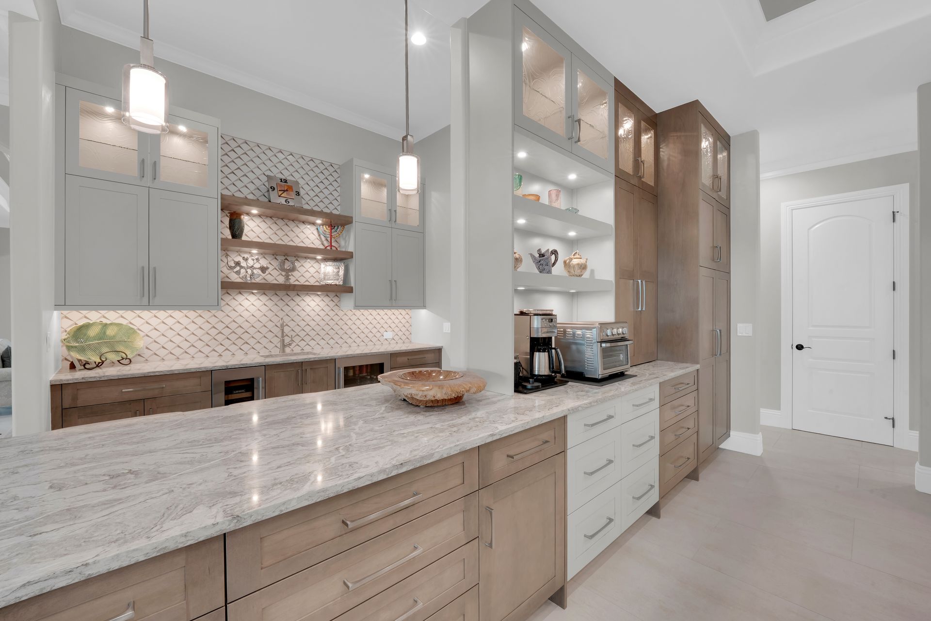 Modern kitchen with light gray cabinets, marble countertops, and built-in appliances.