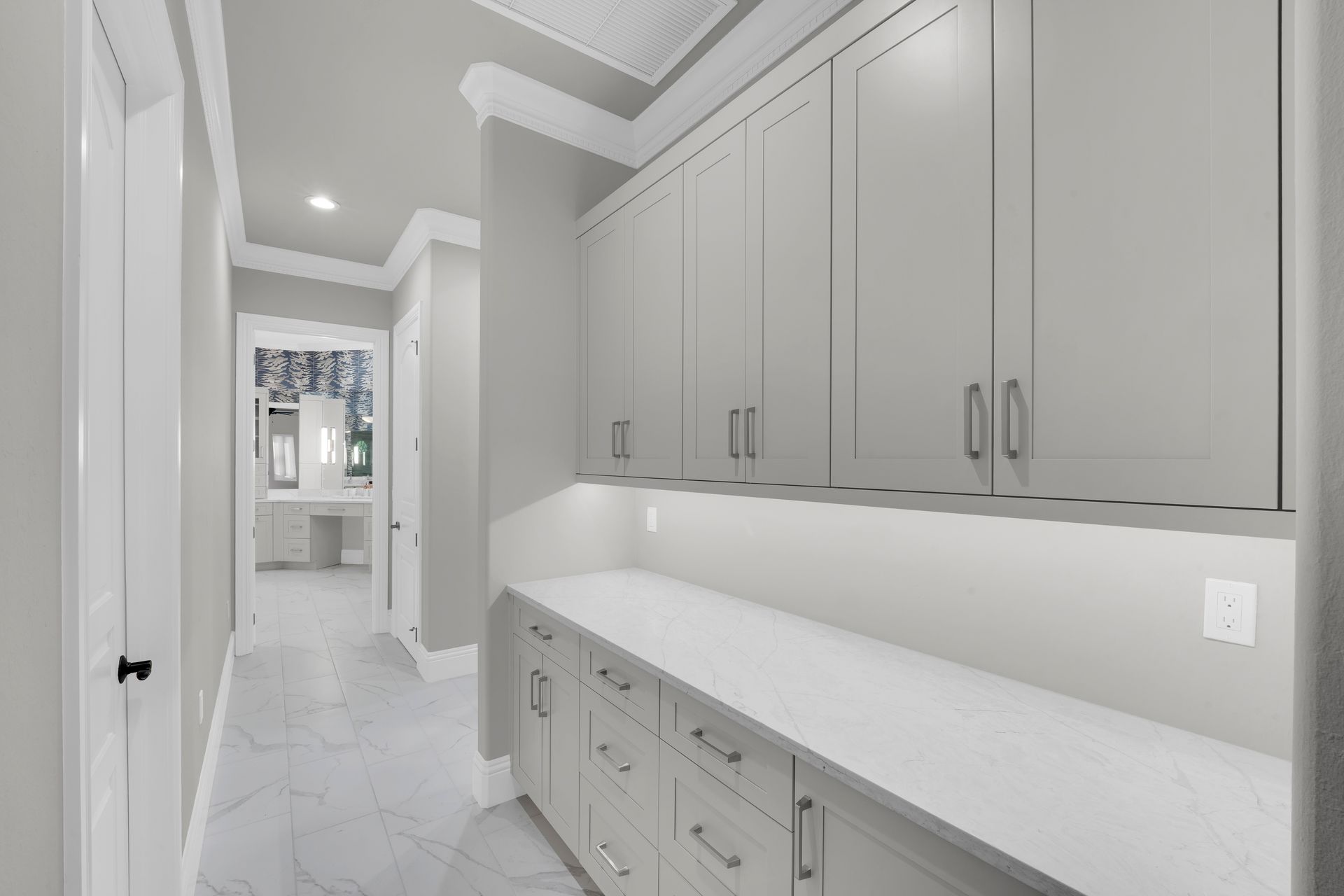 Hallway with light gray cabinets, white countertop, and doorway to a bathroom.