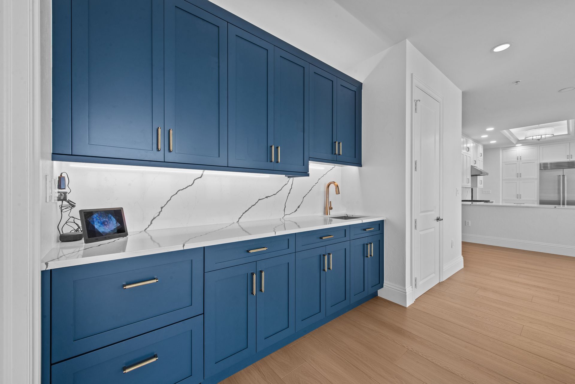 Blue kitchen cabinets with white countertops, sink, and door, and wood floors.