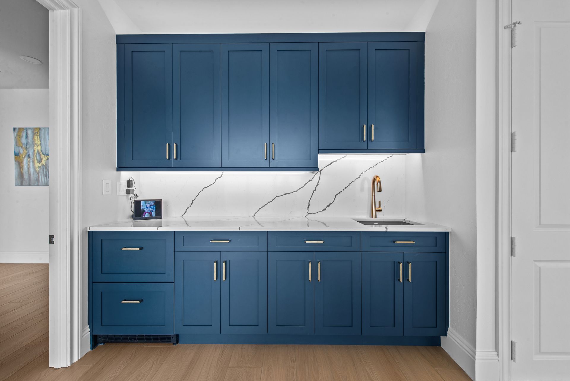 Blue built-in cabinets with a white countertop and a marble backsplash; a small sink and faucet.
