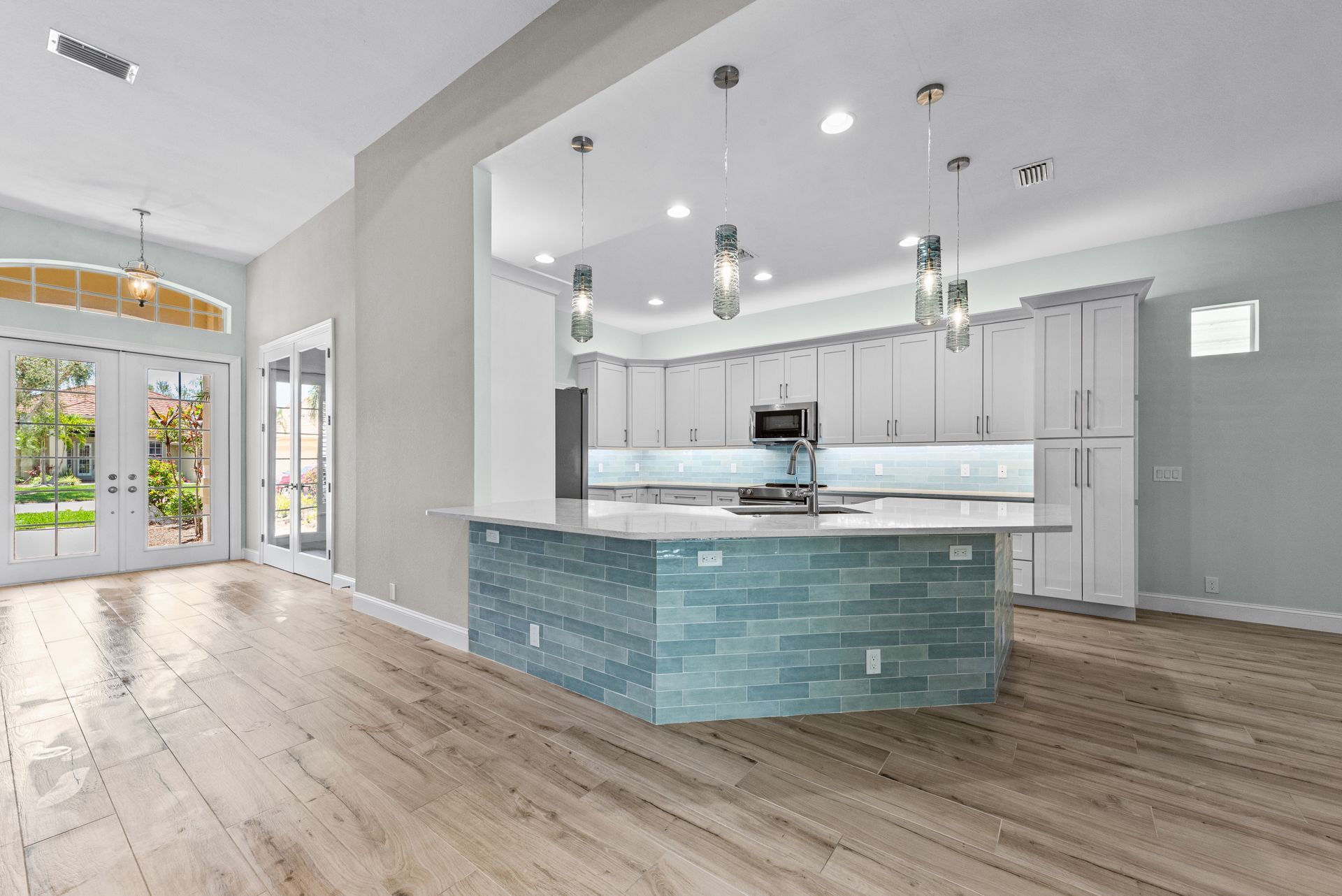 Spacious kitchen with island. Light wood floors, white cabinetry, blue tile on island, and glass pendant lights.