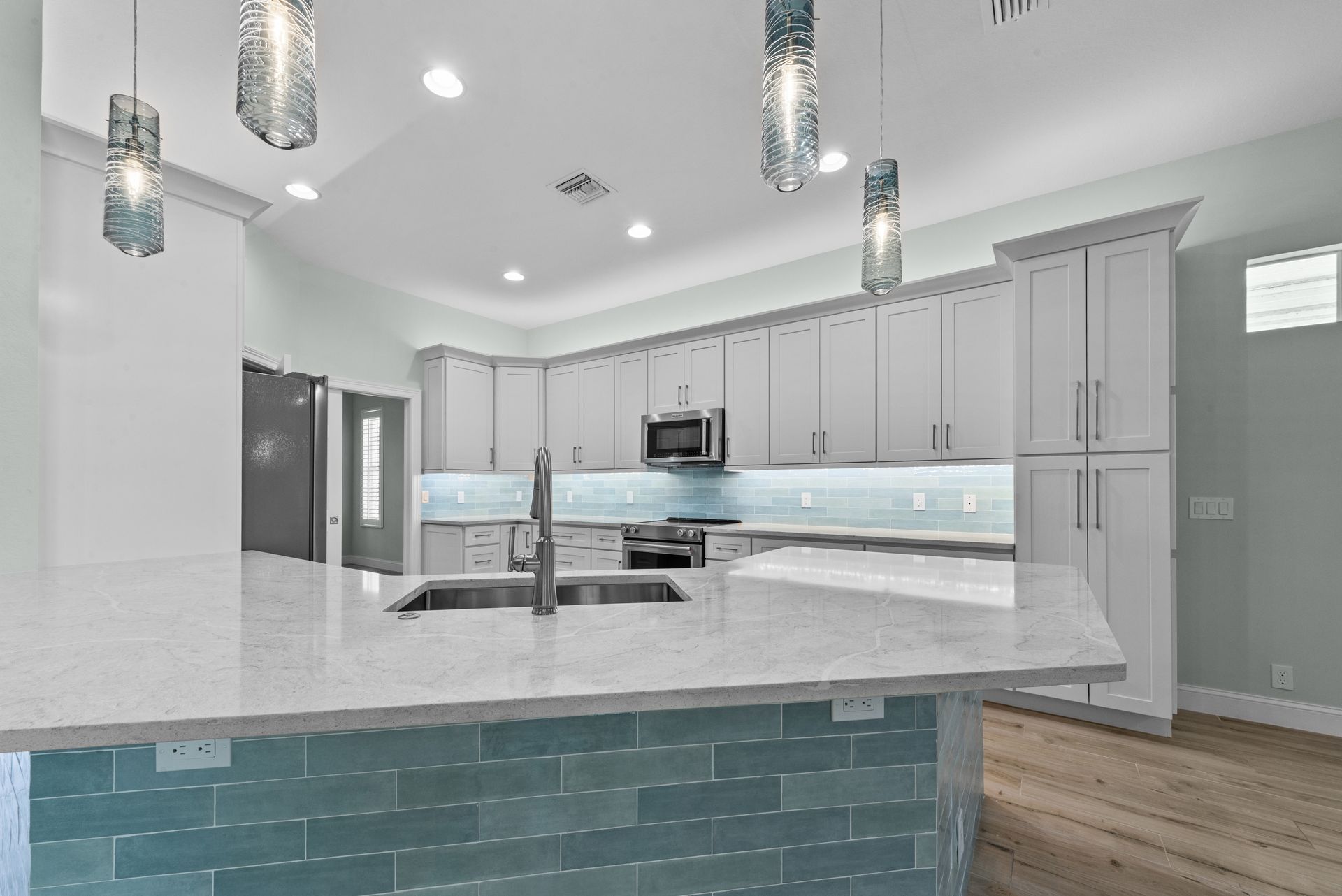 Modern kitchen with light blue cabinetry, quartz countertops, and blue tile accents.