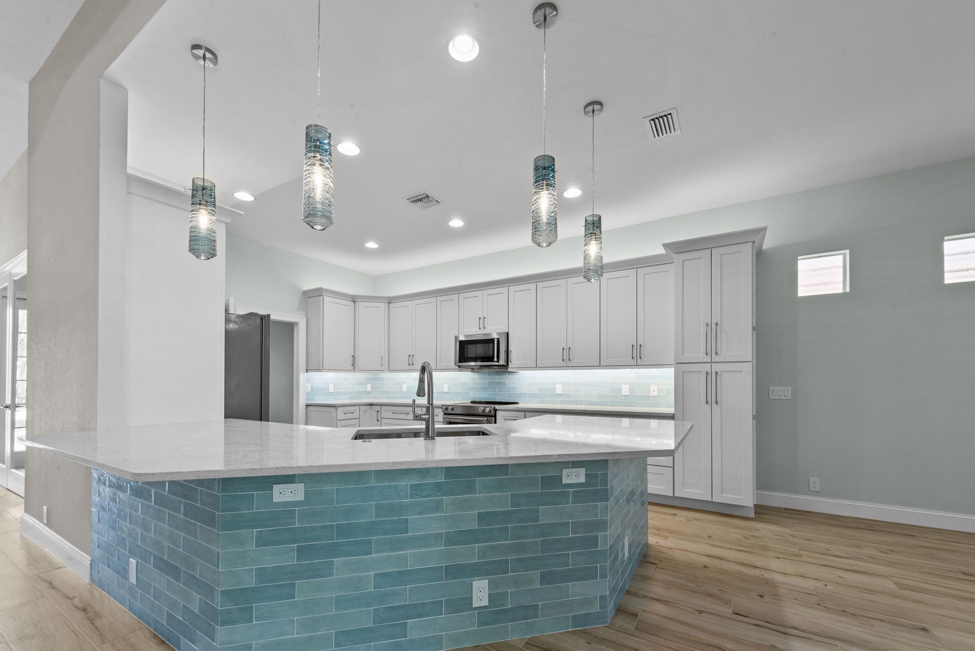 Modern kitchen with white cabinets, blue tile island, and pendant lights.