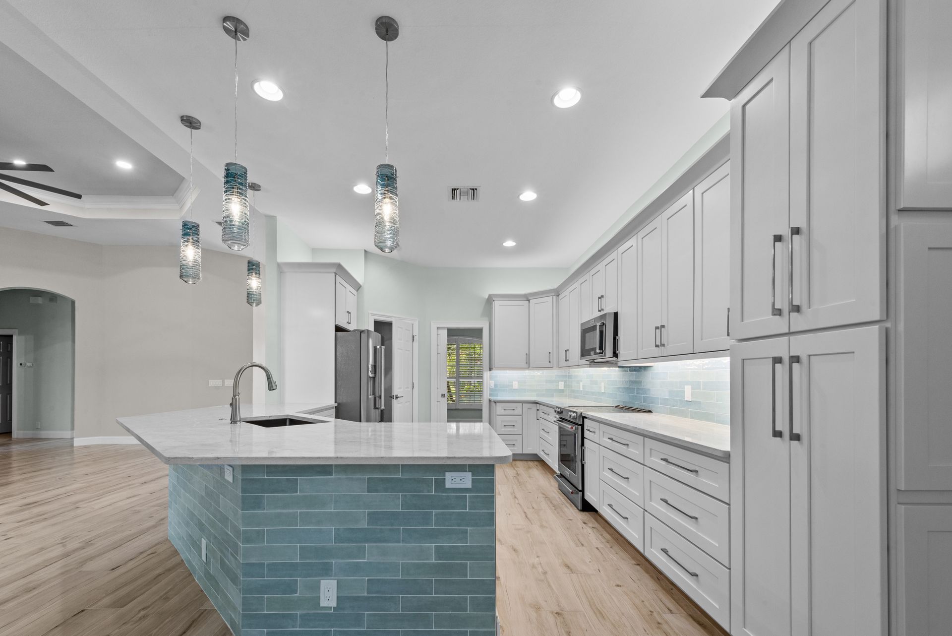 Modern kitchen with white cabinets, blue tile island, and light wood floors.