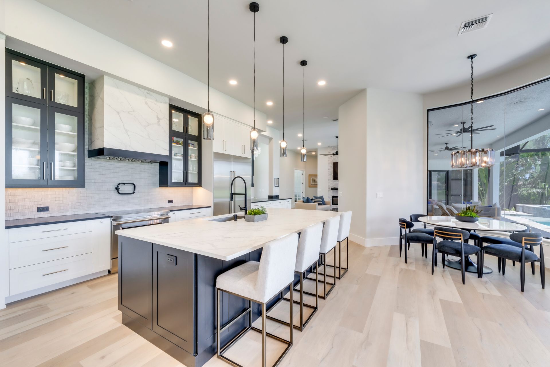 Modern kitchen with white countertops, dark island, and light wood floors. Dining area with large mirror.