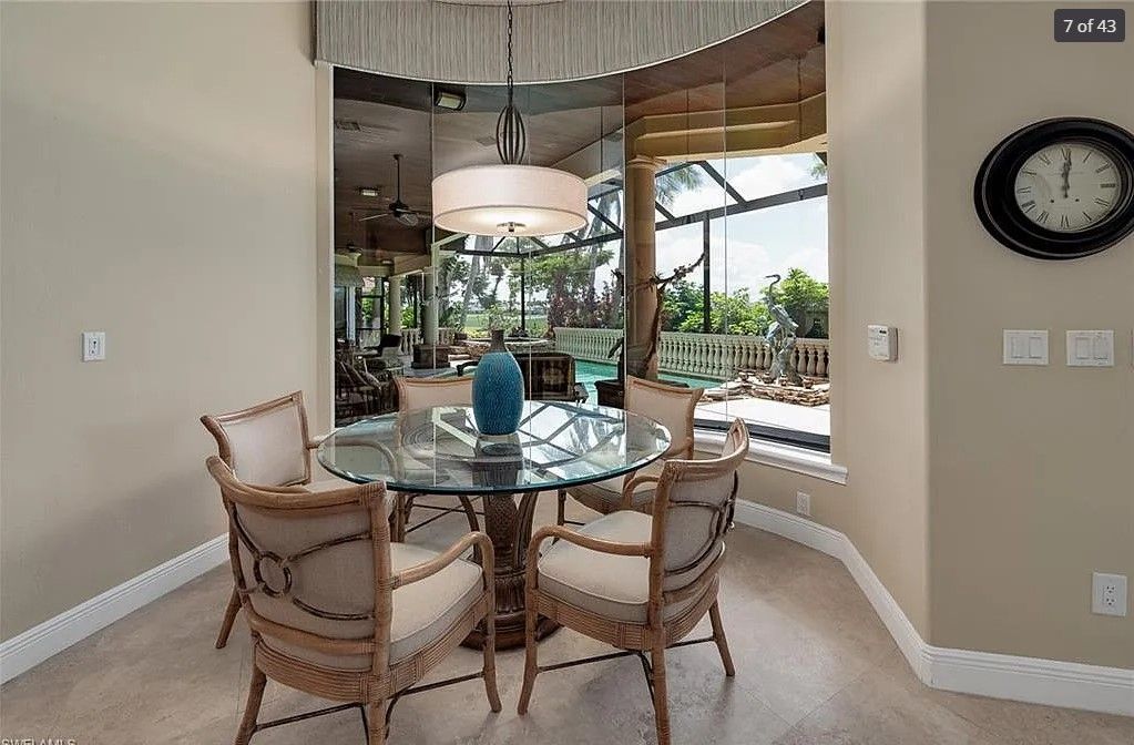 Dining area with glass table and four chairs, looking out to a screened patio and pool.