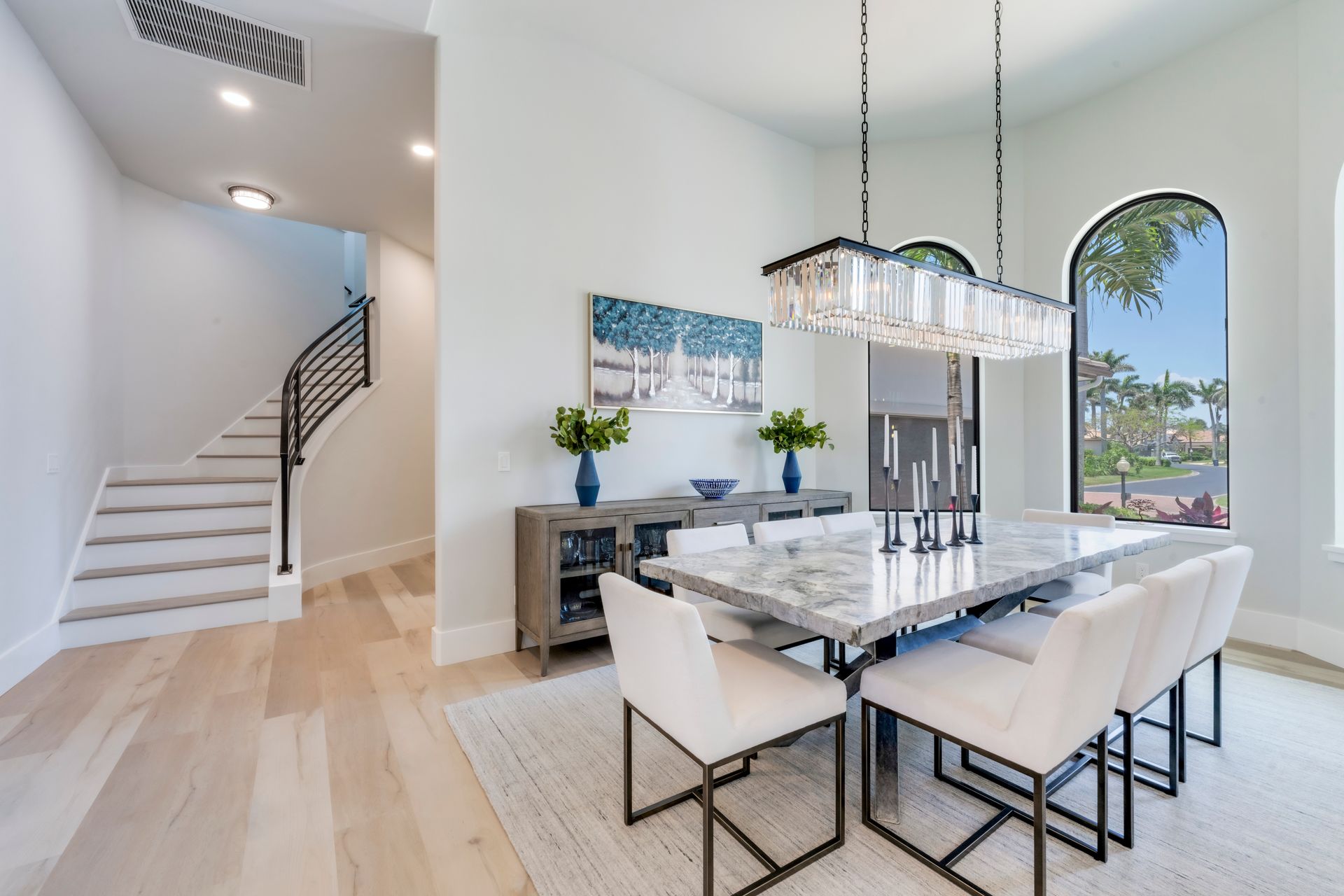 Dining room with marble table, white chairs, and large arched window.