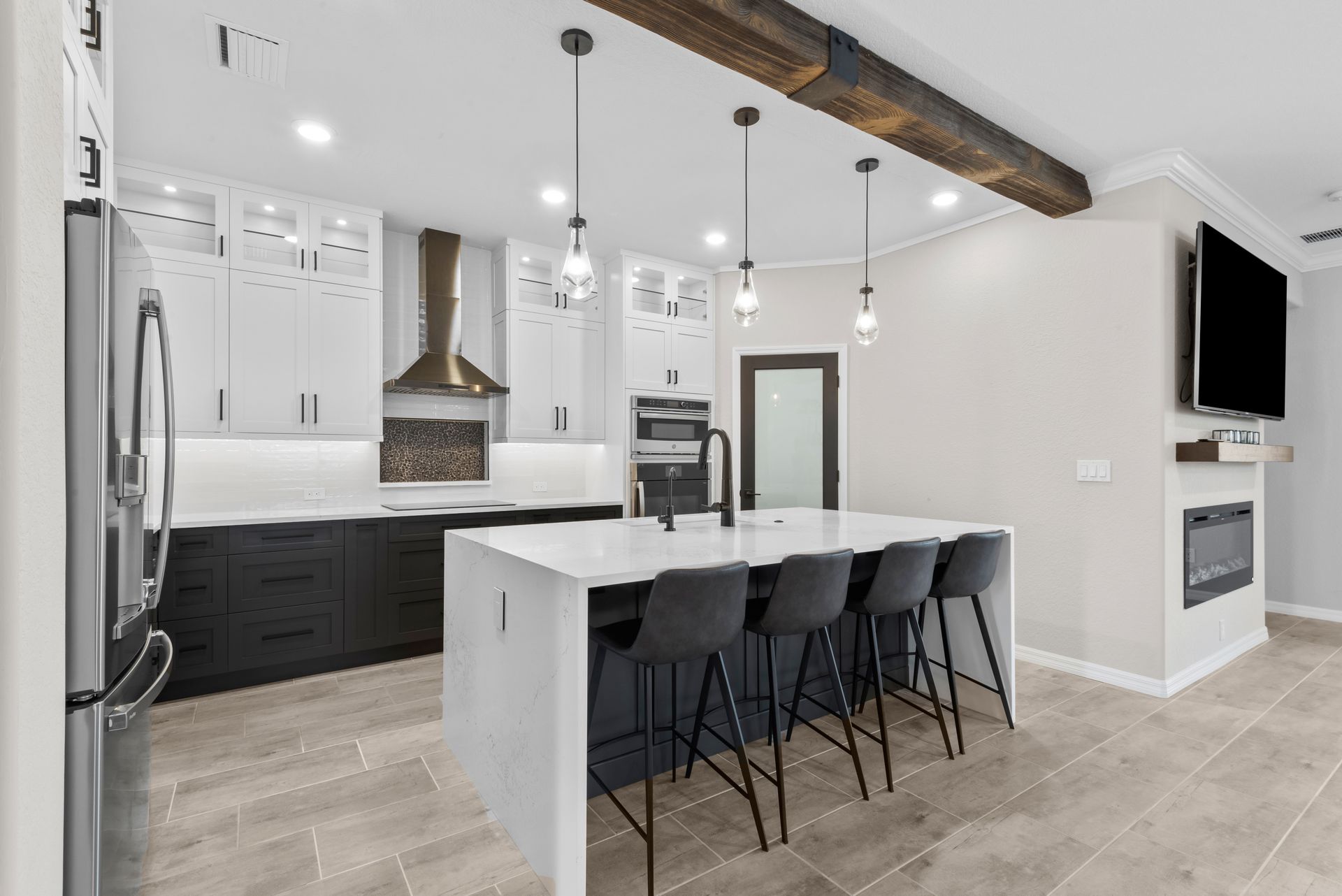 A kitchen with a large island , stools , a refrigerator and a television.
