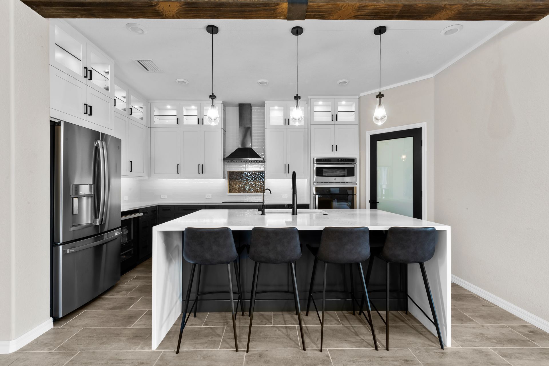 Modern kitchen with white cabinets, dark island with bar stools, stainless steel appliances, and wood beam.