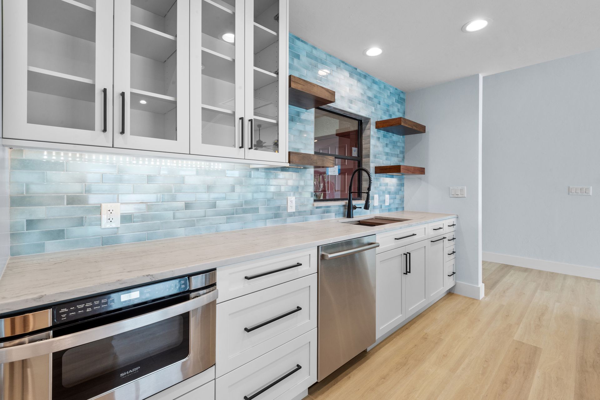 White kitchen with blue tiled backsplash, white cabinets, stainless steel appliances, and wooden shelves.