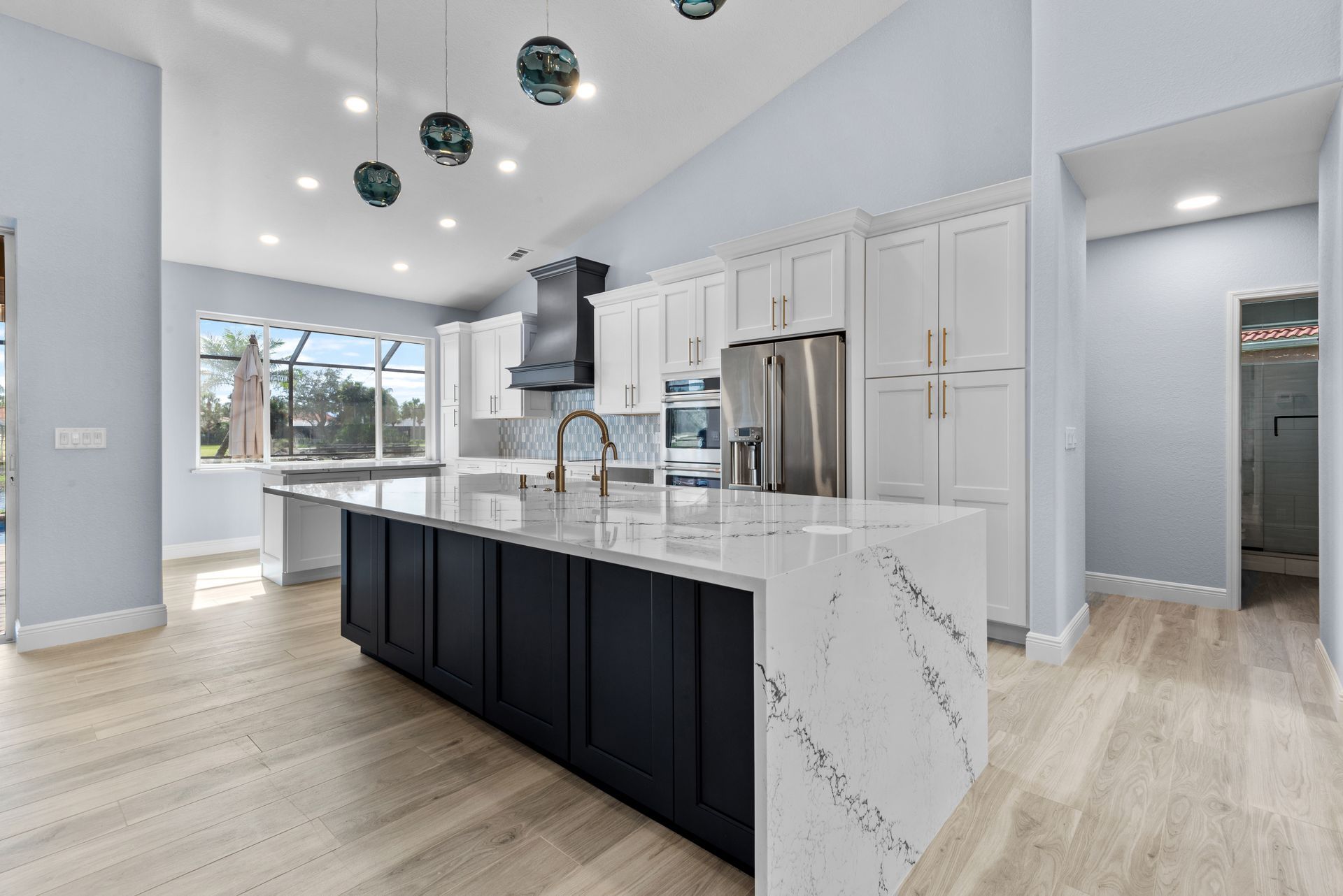 Spacious kitchen with a large island, white cabinets, and stainless steel appliances. Pale blue walls and light wood floors.