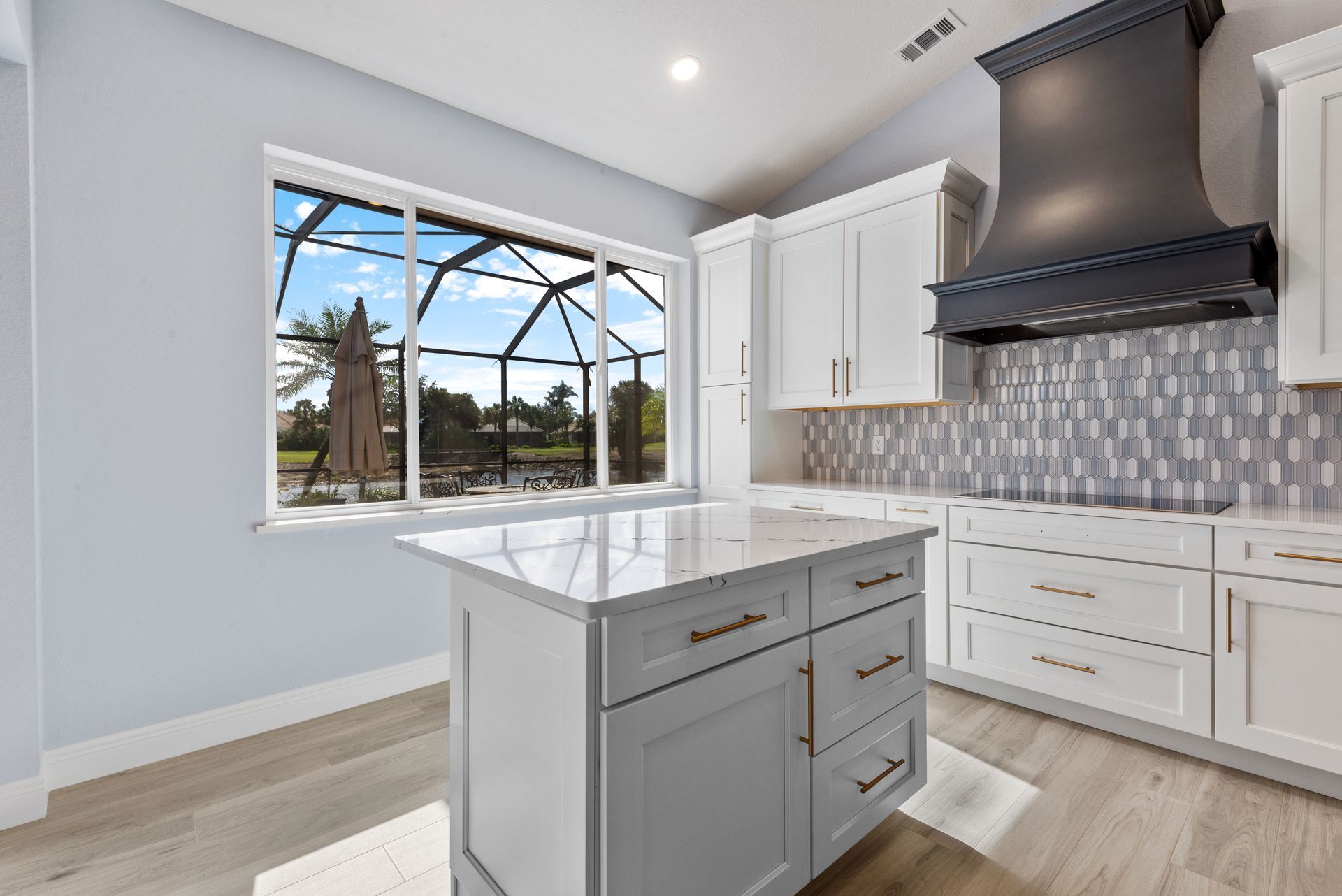 Modern kitchen with white cabinets, gray island, and view of a pool.