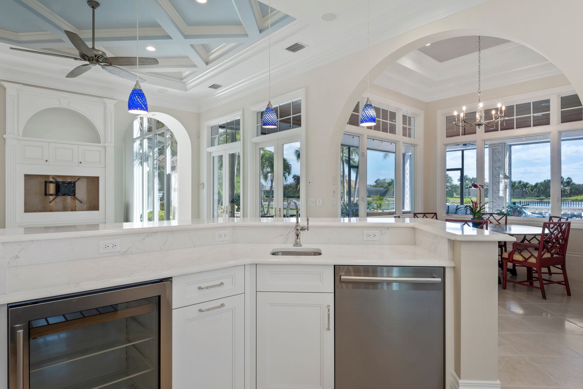 Spacious white kitchen with arched doorways, large windows, a bar, and a dining area overlooking a waterfront view.