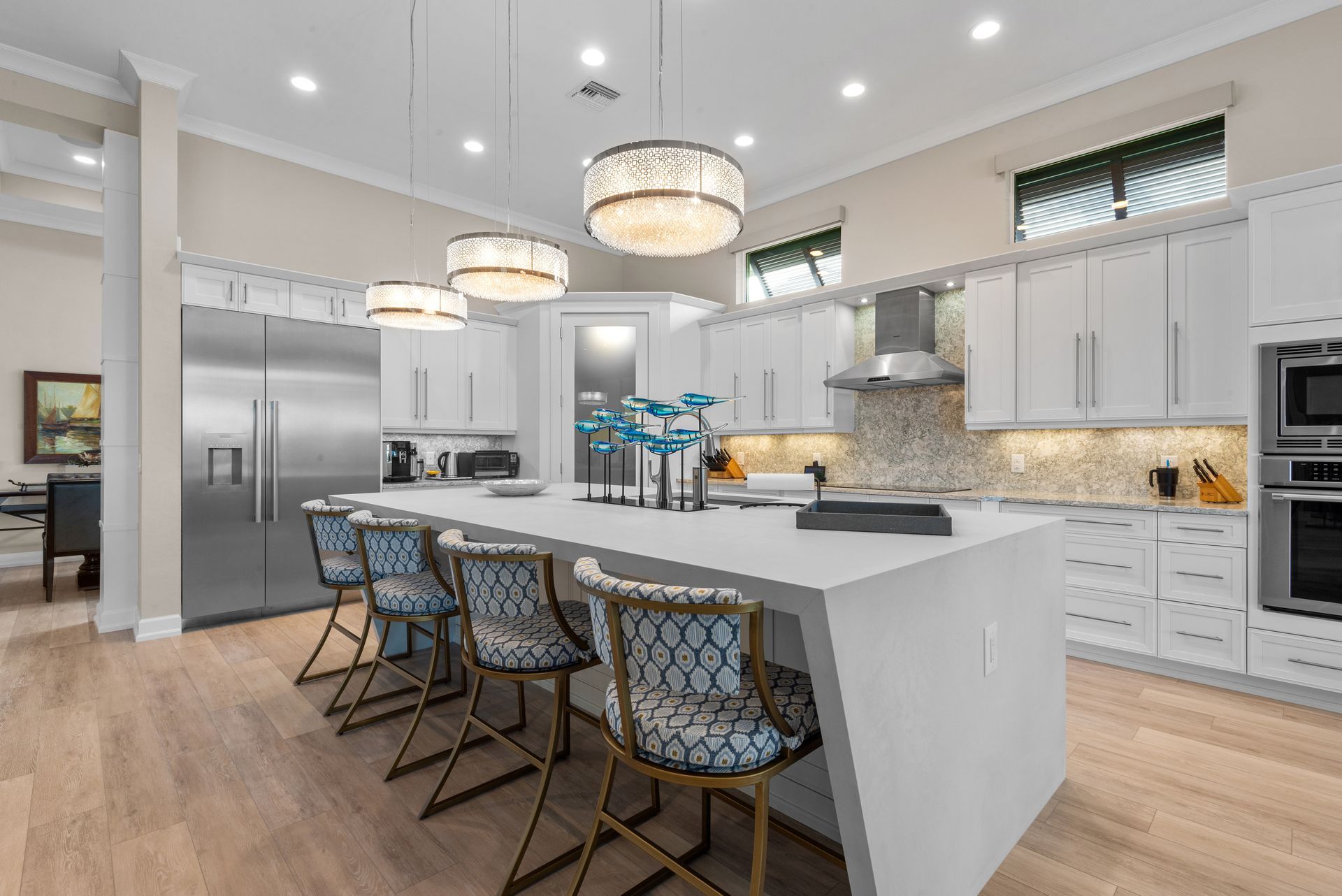 Modern kitchen with white cabinets, island with stools, stainless steel appliances, and pendant lights.