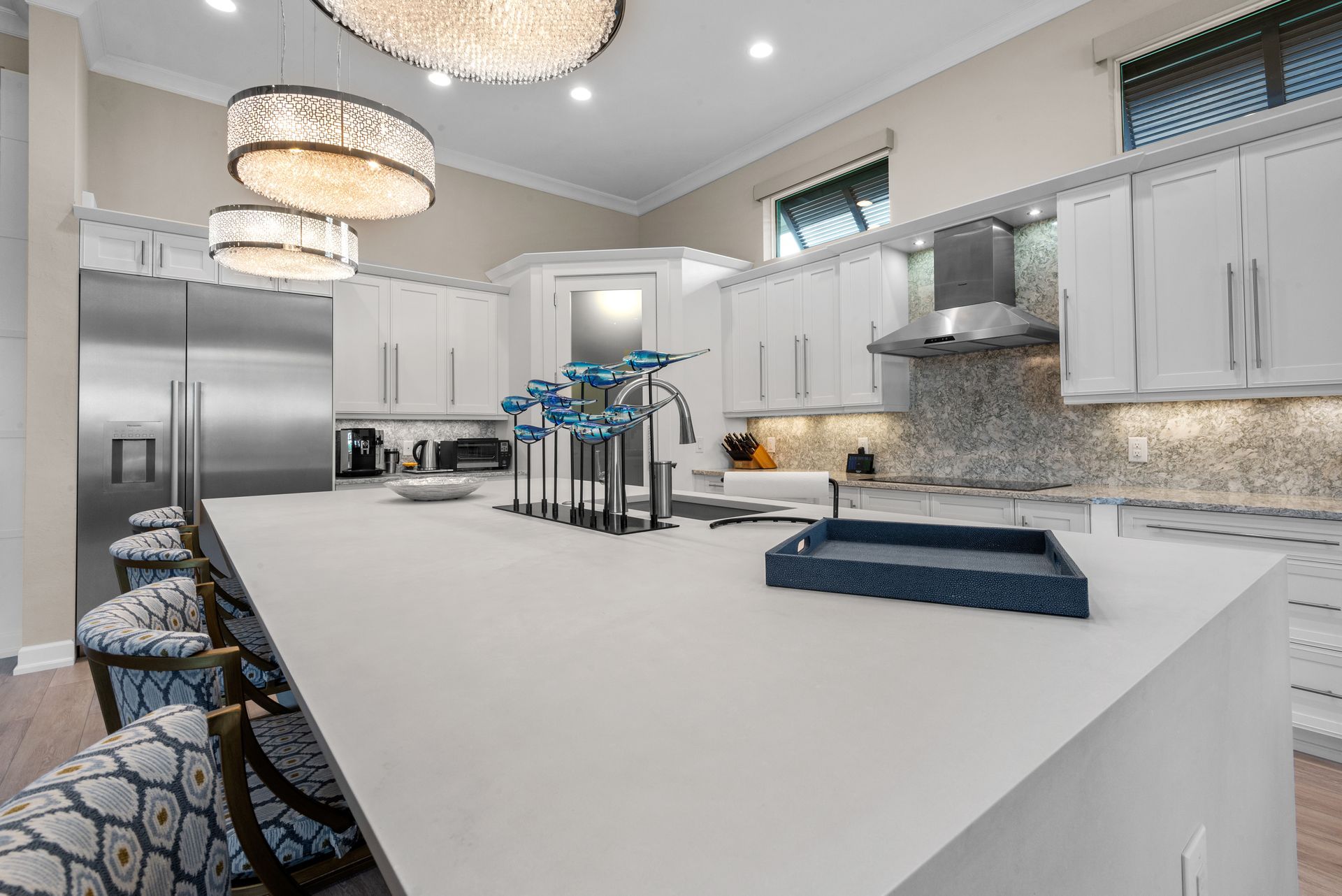 Modern white kitchen with island, pendant lights, stainless steel appliances, and seating.