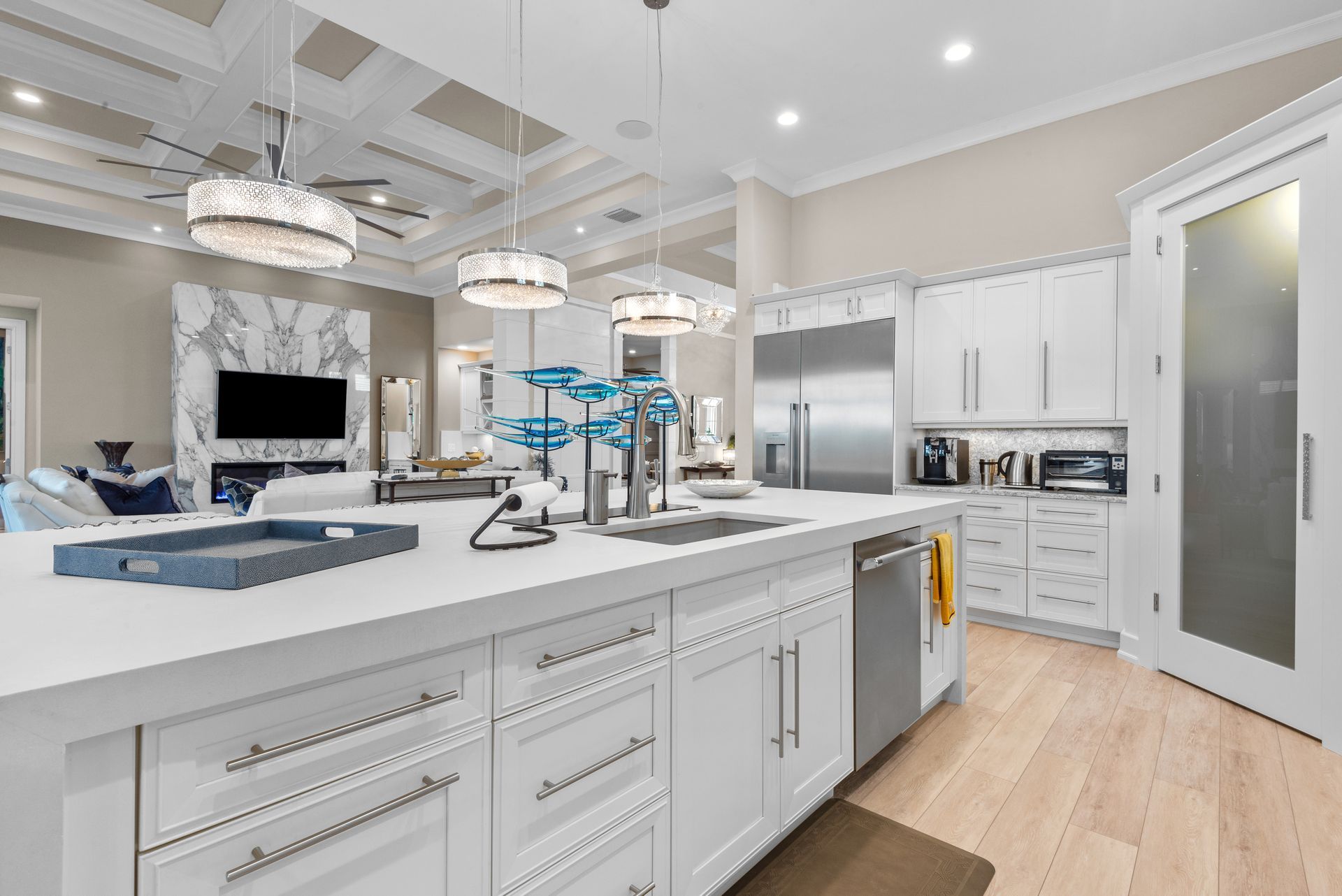 Spacious white kitchen with island and stainless steel appliances; living area with fireplace visible in background.