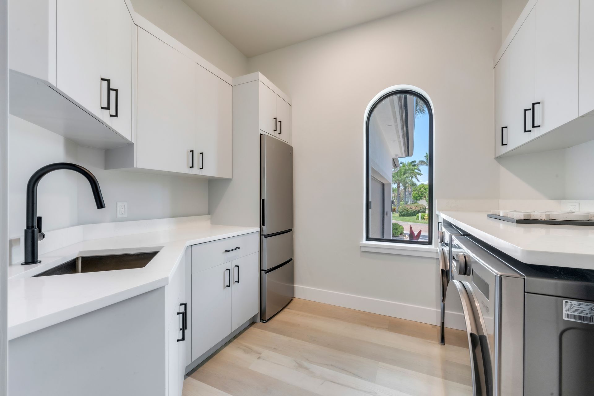 Modern laundry room with white cabinets, stainless steel appliances, and arched window.