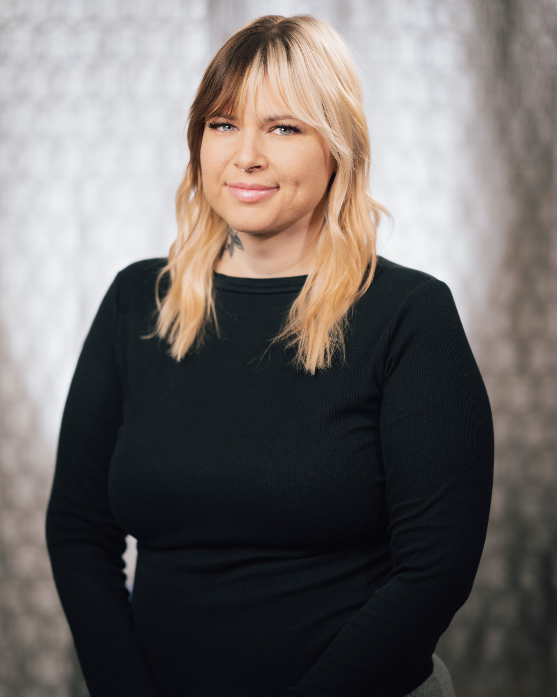 A woman with blonde hair and a black shirt is standing in front of a window.
