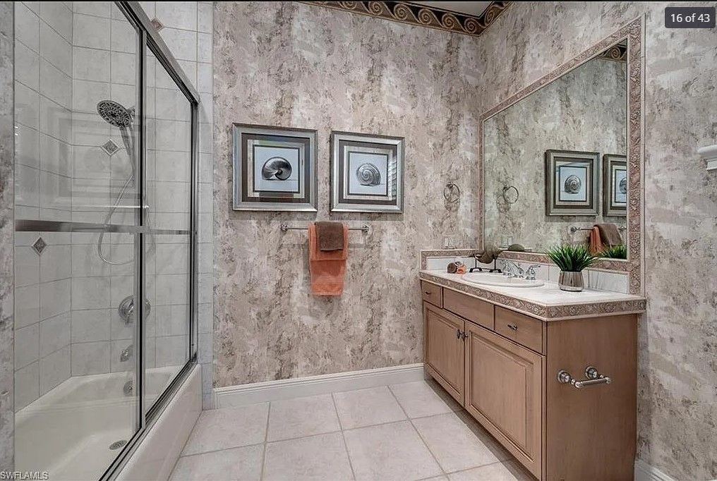 Bathroom with shower, vanity, and marble-patterned walls and floor. Beige cabinetry and framed mirror.