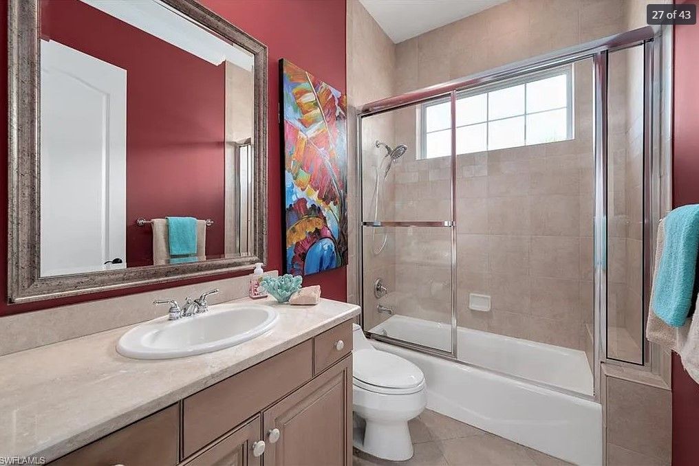 Bathroom with red wall, vanity with sink, mirror, art, tub/shower, and toilet.