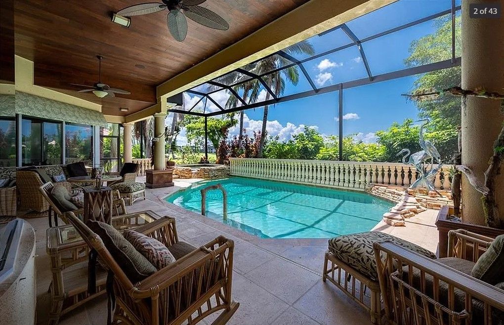 Screened-in pool area with seating, overlooking trees and a bright blue sky.