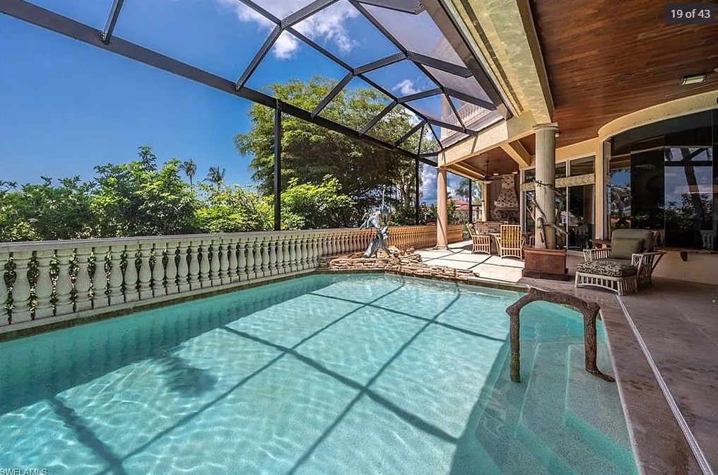 Swimming pool under a screened enclosure with decorative fencing, a fountain, and trees.