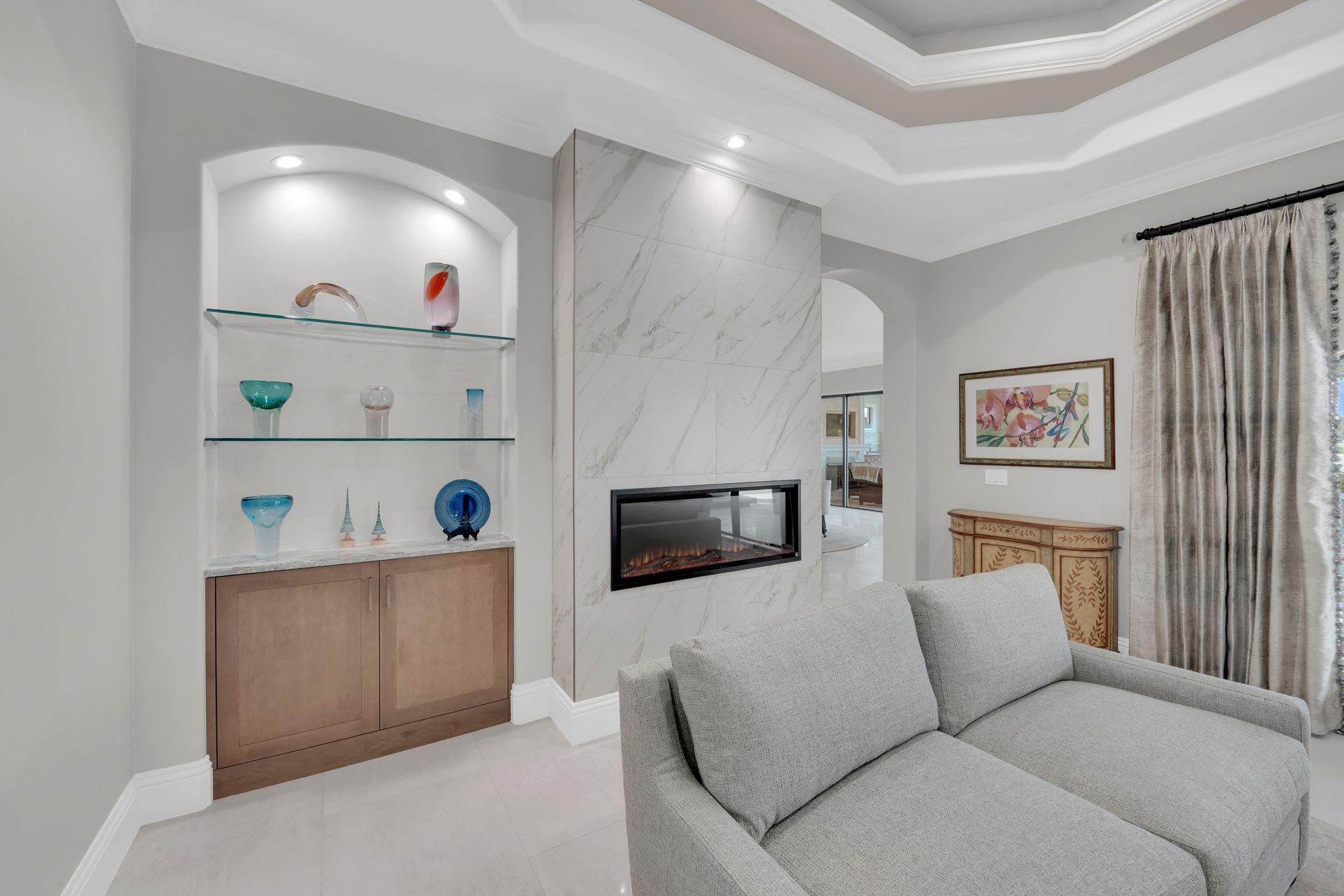 Living room with fireplace, built-in shelving, and sofa. White marble fireplace, neutral walls, and light-colored sofa.