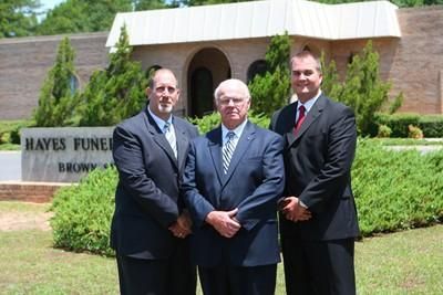 Three men in suits standing outside Hayes Funeral Home on a sunny day