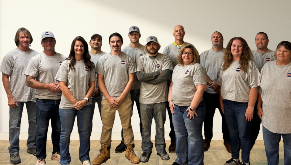 Group of people in gray shirts and hats, posing in front of a white wall.