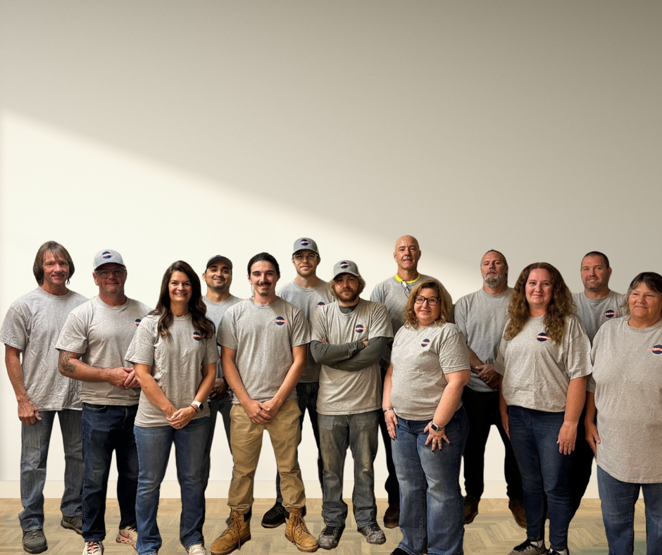 Team of 14 people wearing gray shirts and baseball caps, standing in front of a white wall.