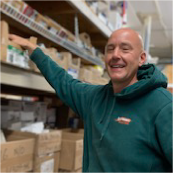 Man in green hoodie, reaching for item on a shelf in a store, smiling.