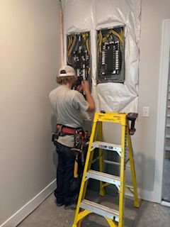 Electrician working on electrical panels in a room, using a yellow ladder.