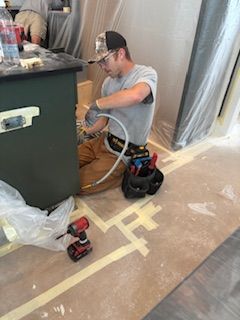 Man in work clothes installing plumbing, kneeling, tools nearby.