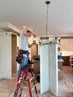 Person installing a chandelier, standing on a red ladder in a room under construction.