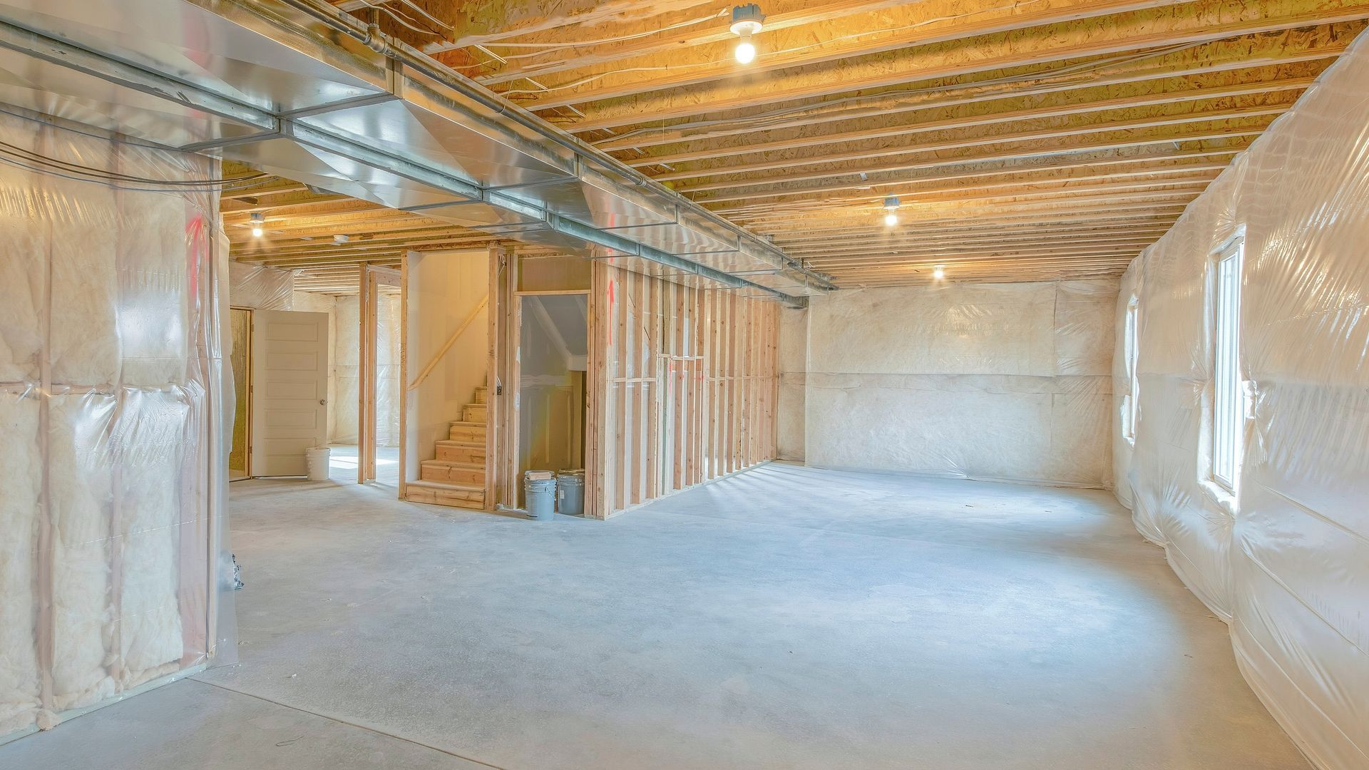Unfinished basement interior with exposed ceiling beams, insulation walls, and concrete floor