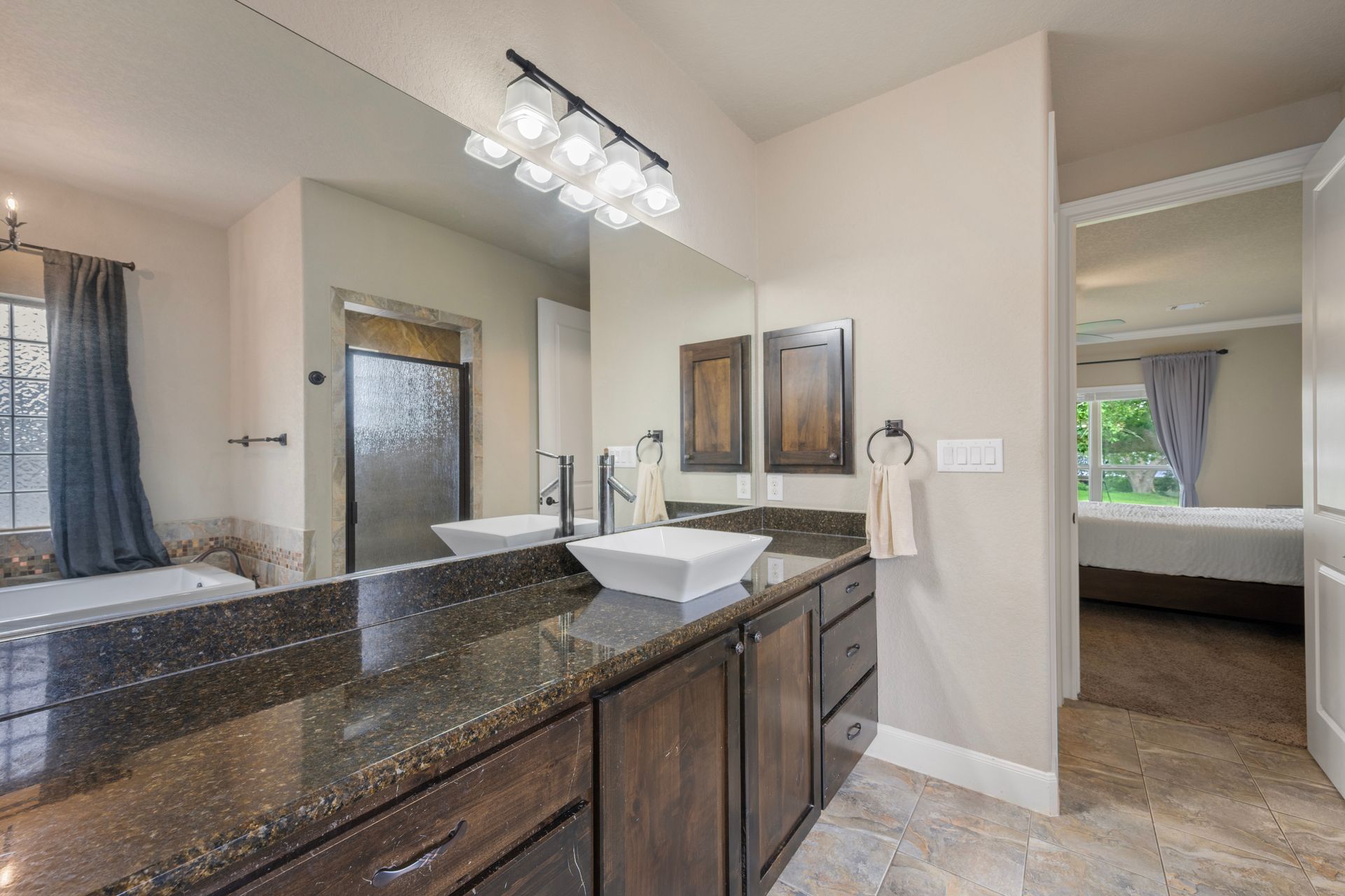 Spacious bathroom with double vanity, granite countertop, mirrors, and adjoining bedroom doorway.
