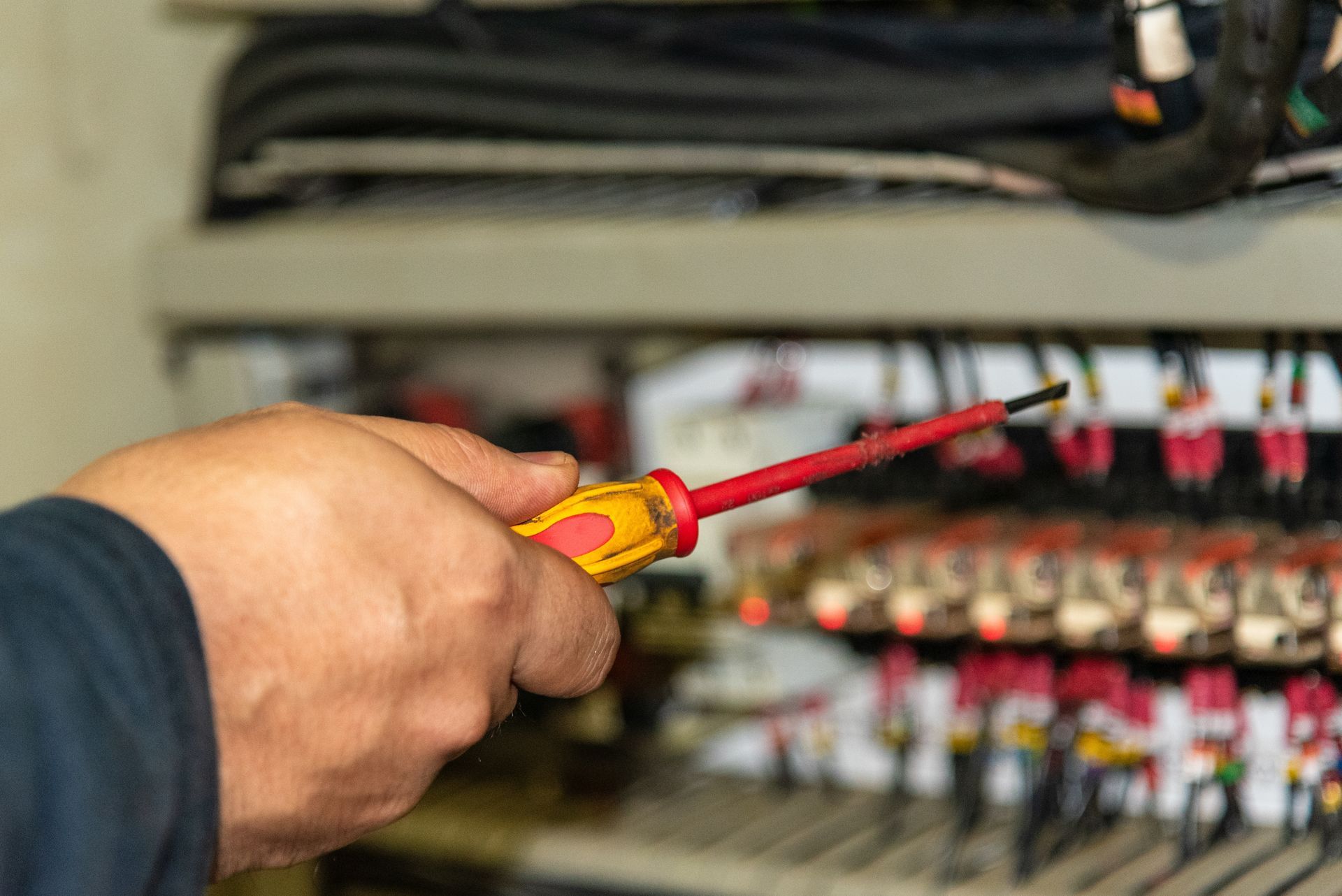 Hand holding a red-and-yellow screwdriver near electrical wiring in a control panel