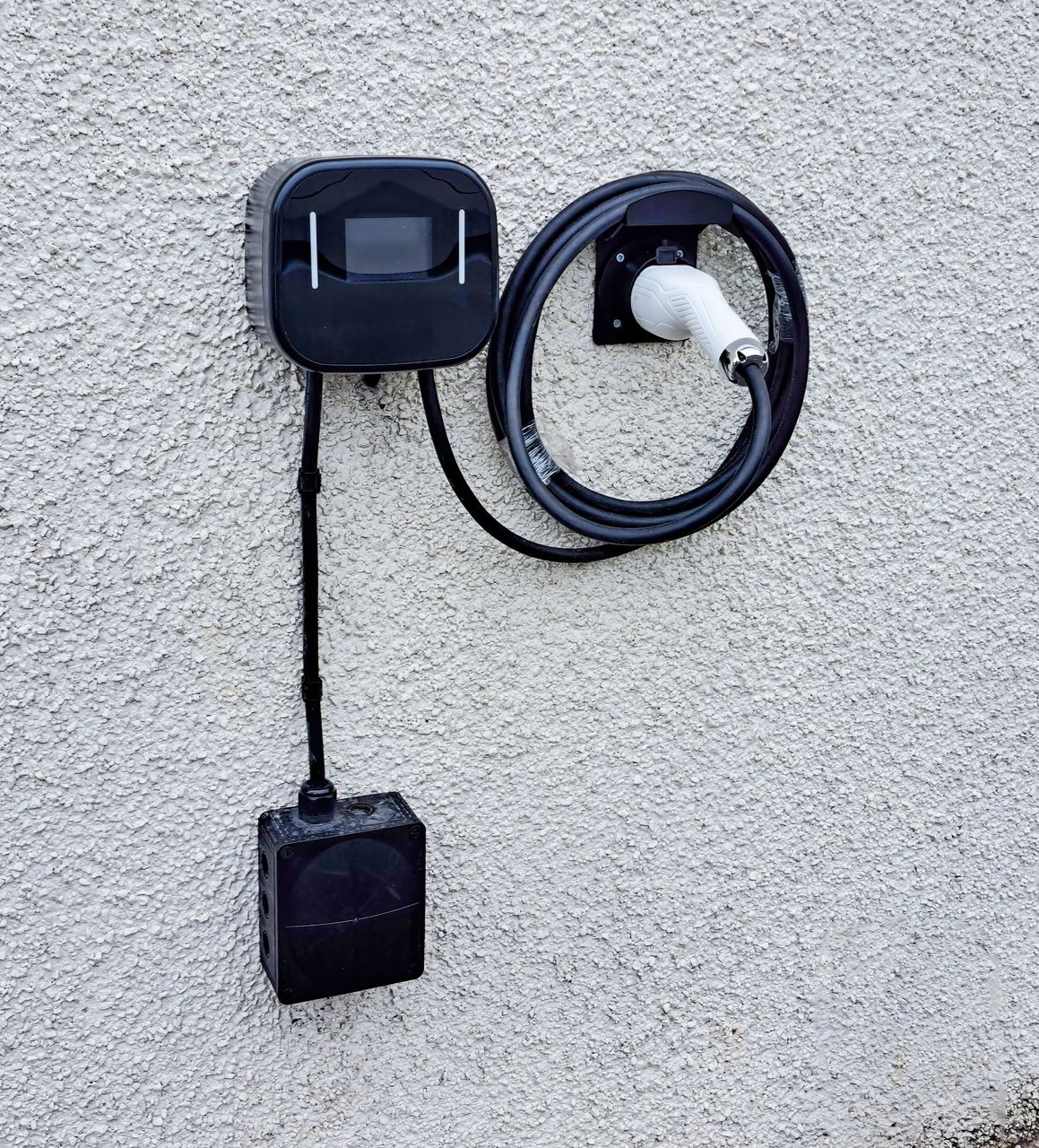 Outdoor wall-mounted EV charging station with a coiled cable and black charging box on a stucco wall