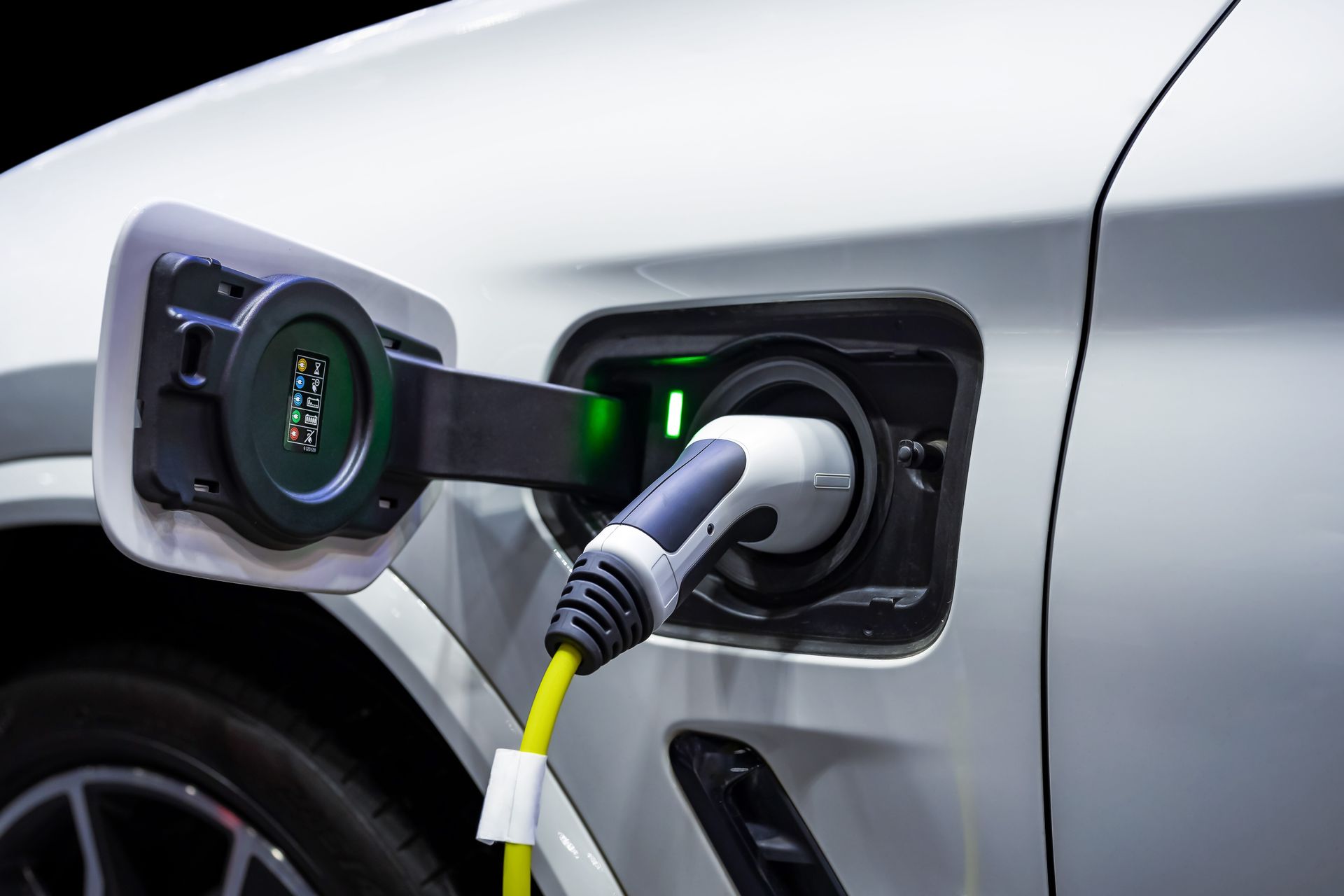 Electric car charging at a plug-in port on a silver vehicle with a green indicator light