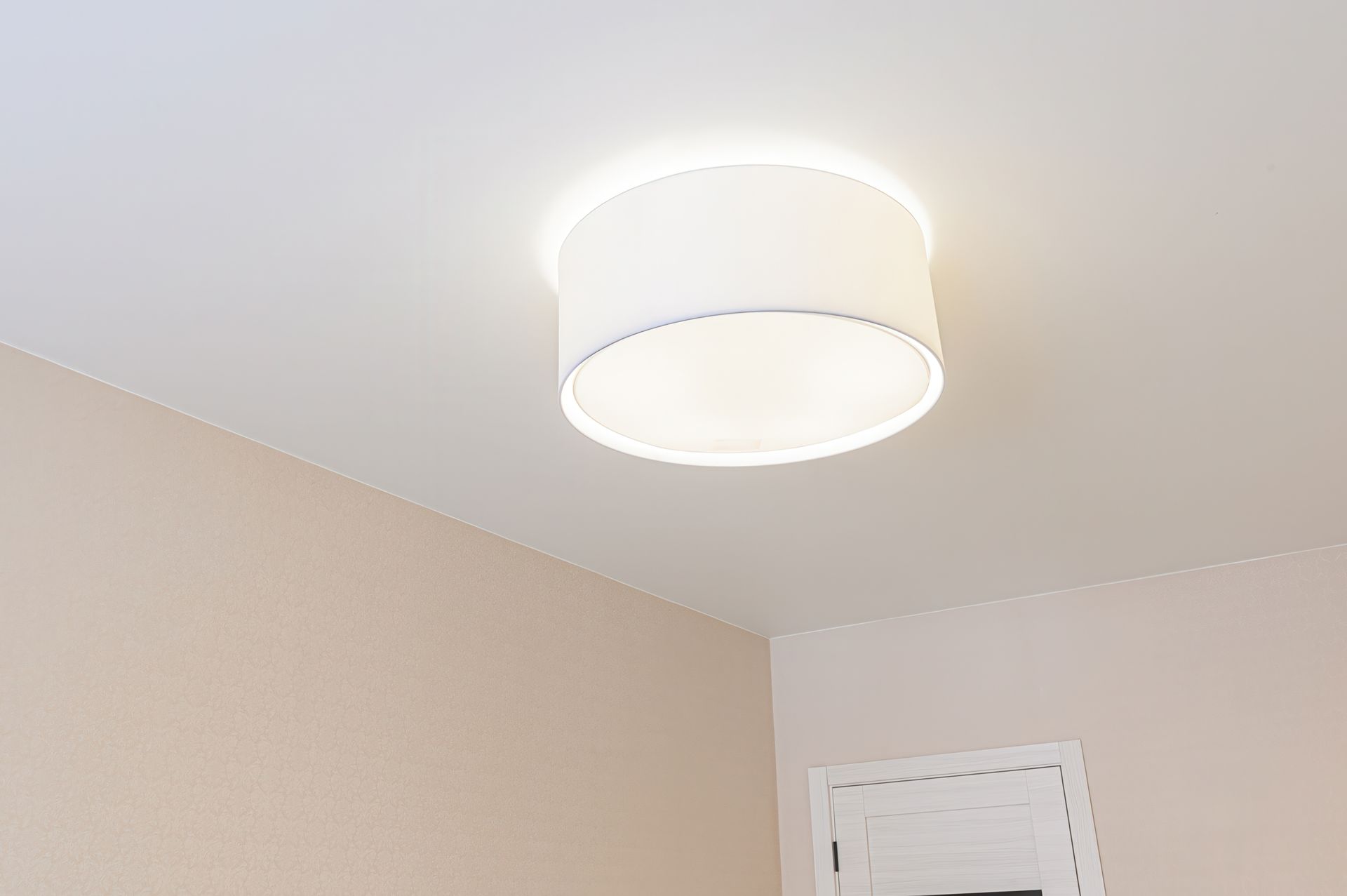 White ceiling light in a beige room corner above a doorway, lit on the ceiling