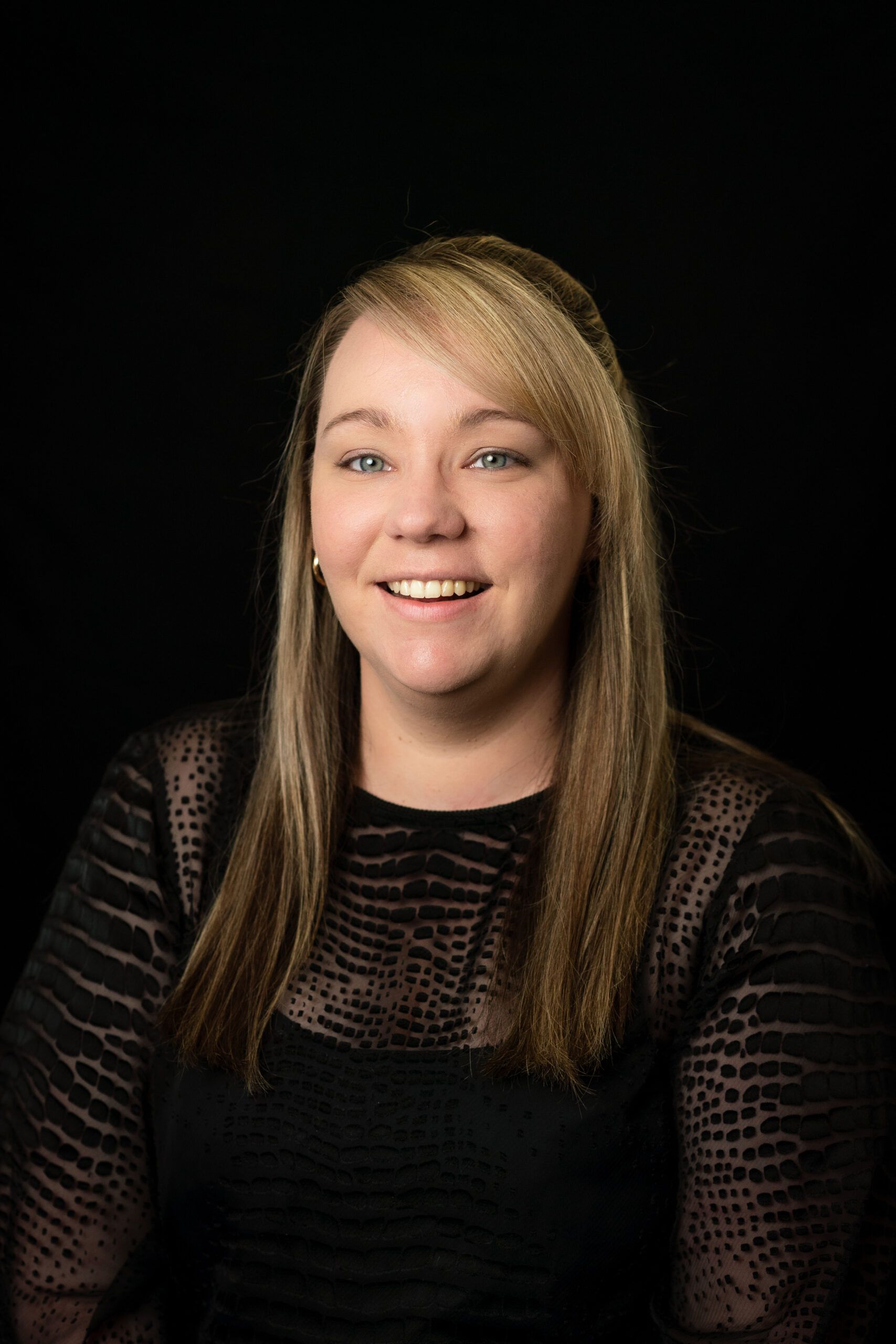 Smiling woman with long blonde hair wearing a black top against a dark background