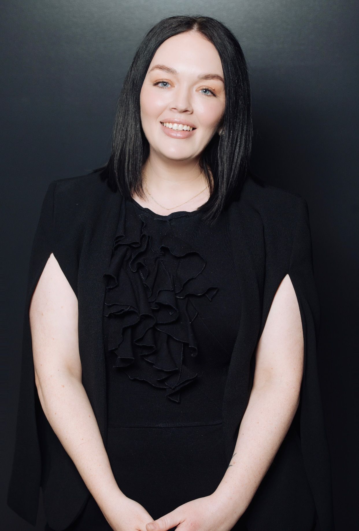 Woman in a black dress smiling against a dark background