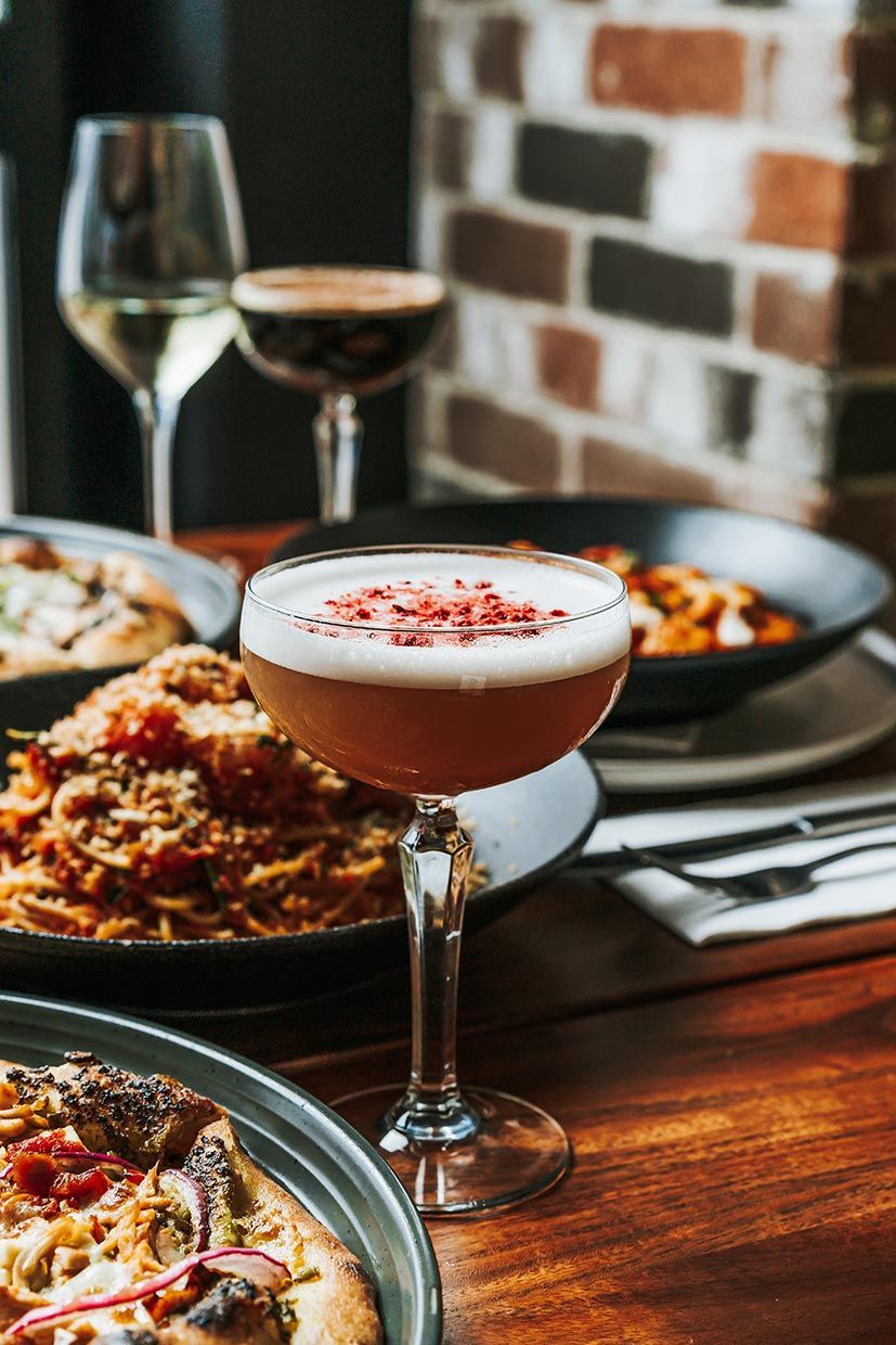 A Glass of Wine is Sitting on a Table Next to a Plate of Food — Fedeles East Gosford in East Gosford, NSW