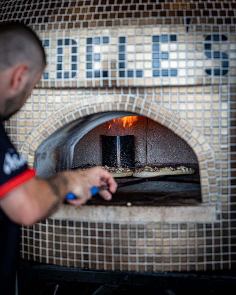 A Man is Putting a Pizza Into a Pizza Oven — Fedeles East Gosford in East Gosford, NSW