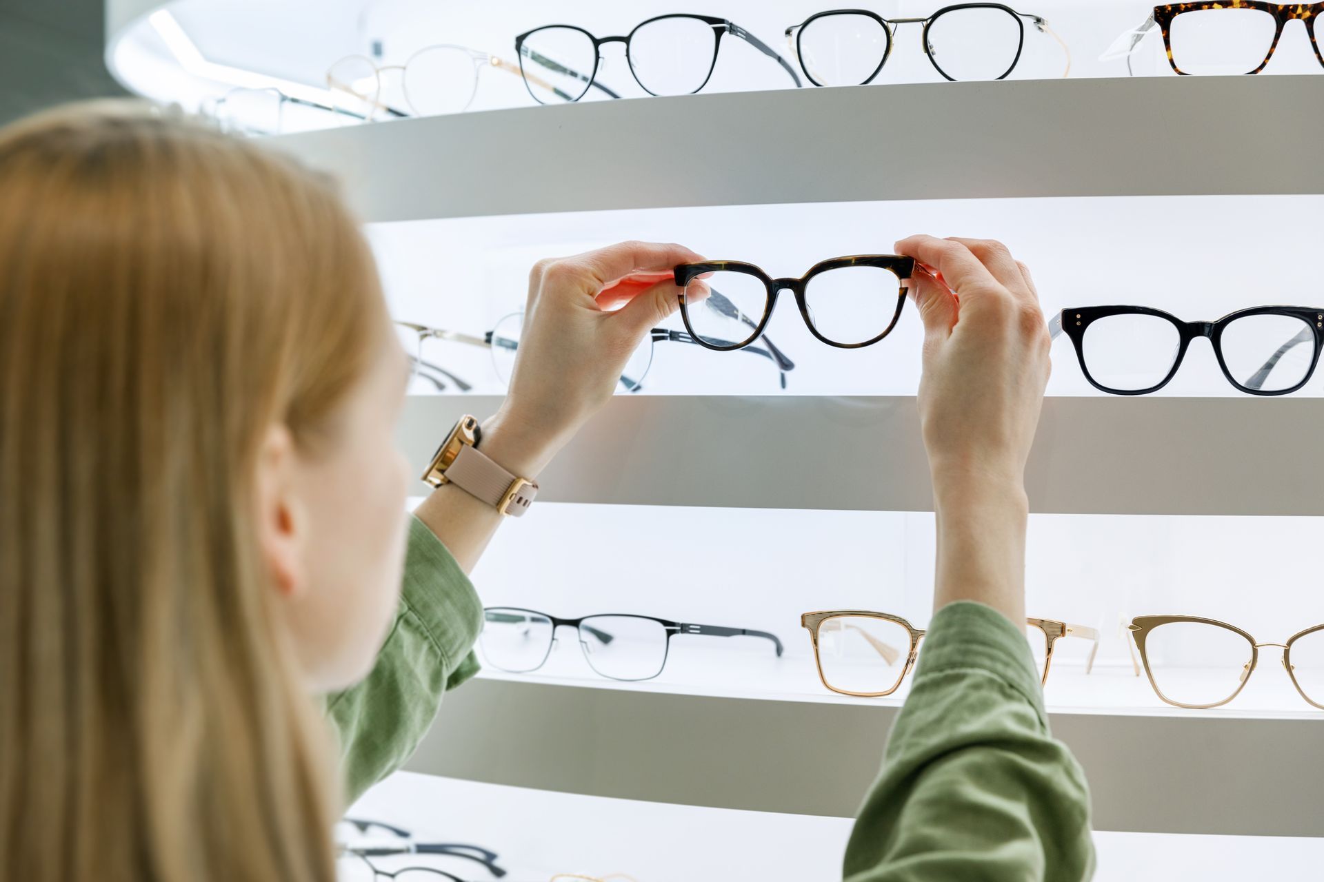 Woman picking eyeglasses from a shelf in an optics store