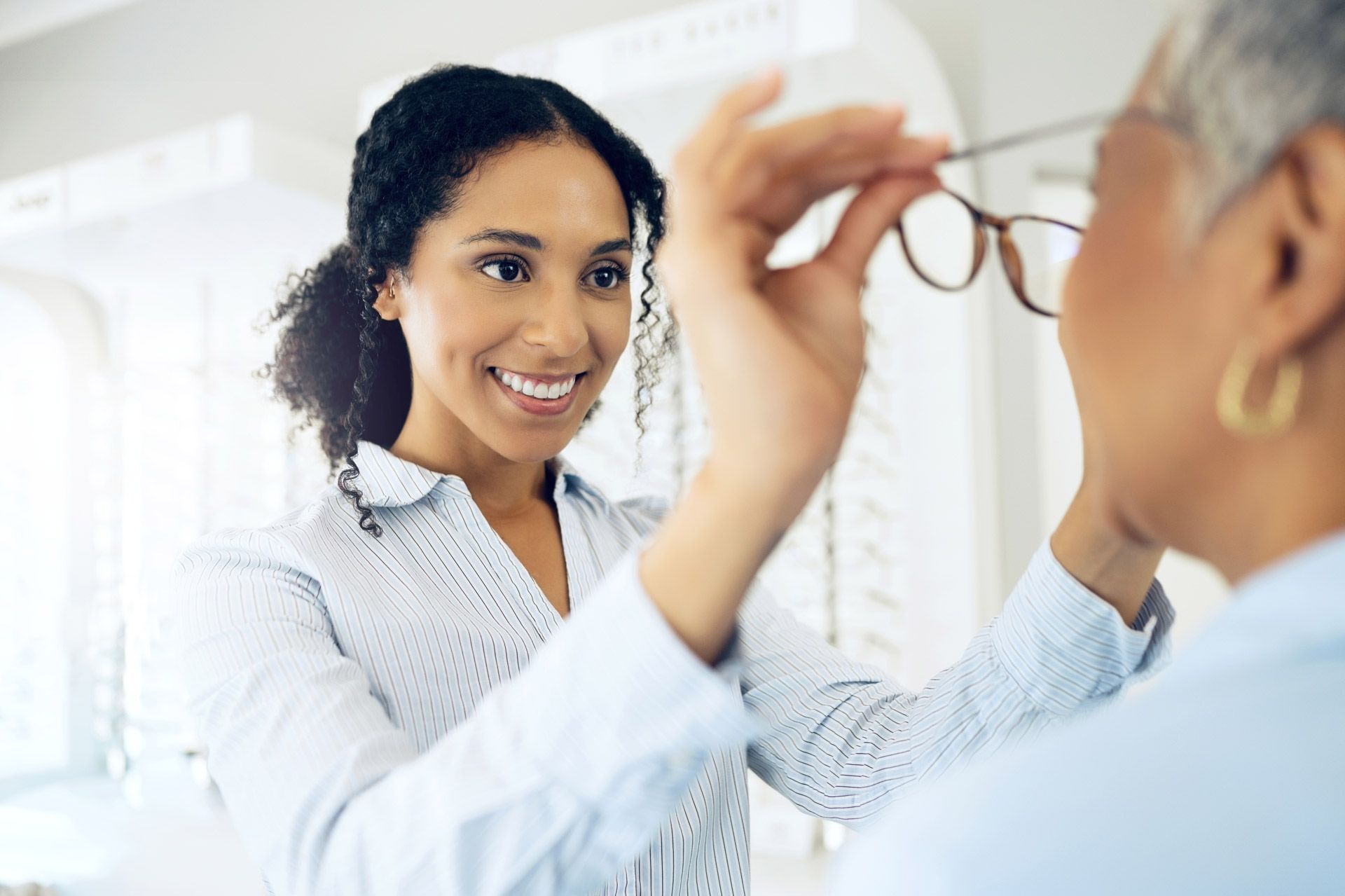 A woman is putting some glasses on a senior woman.