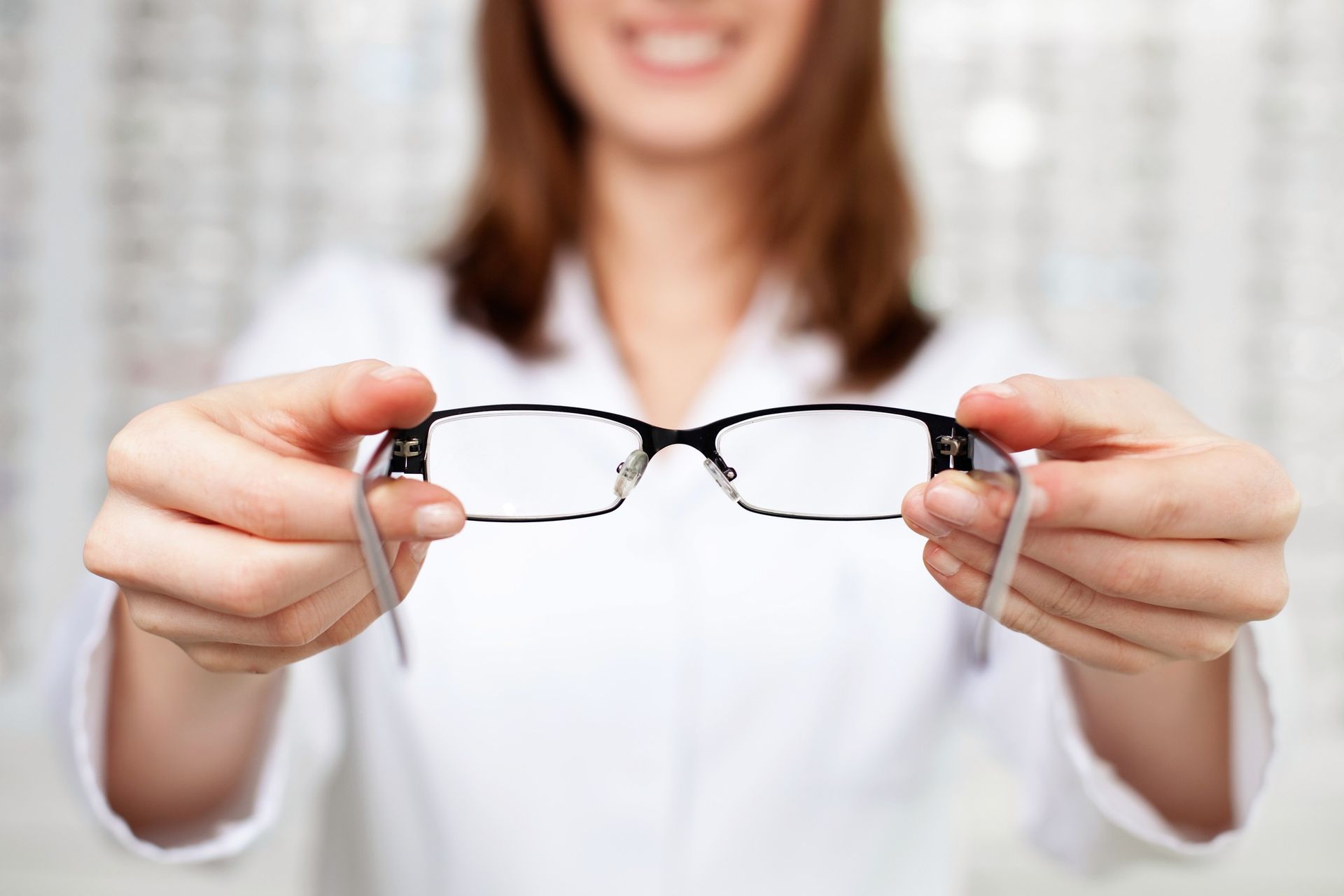 Person holding a pair of eyeglasses toward the camera in a bright indoor setting