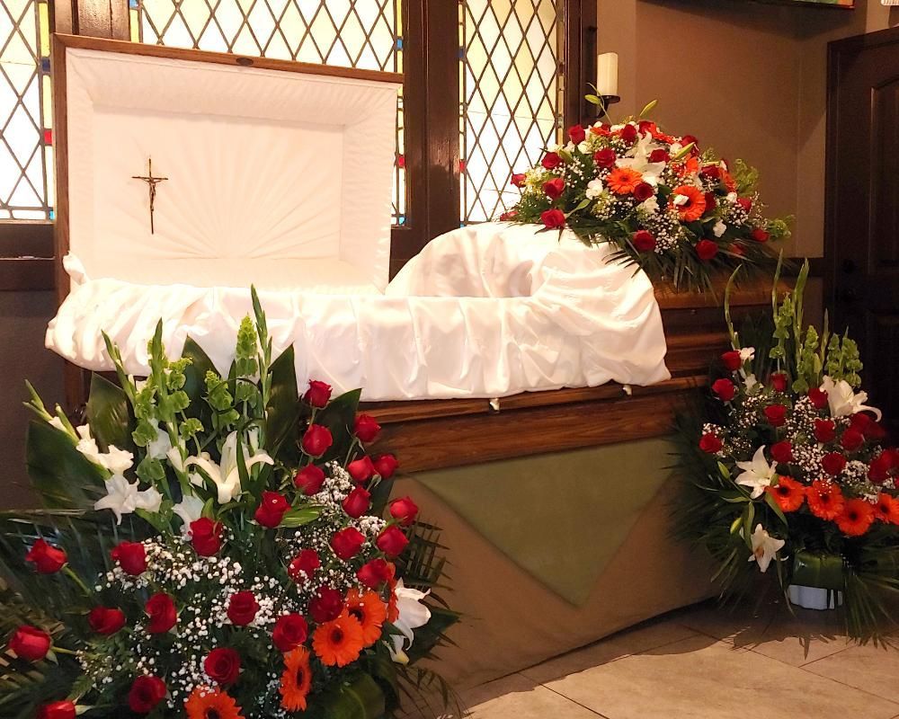 Open casket with white lining, cross, and floral arrangements in a church.
