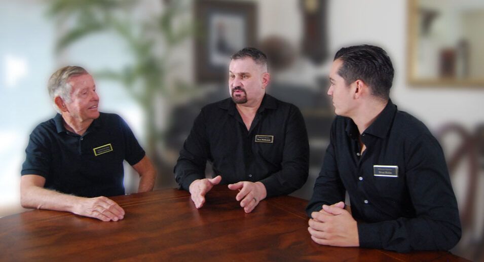 Three men in black shirts smiling in front of a white background.
